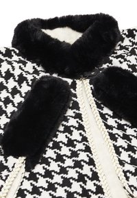 Capa cu model houndstooth, cu guler și accente din blană sintetică neagră. Prezintă margine împletită din aur și închidere cu cârlig.