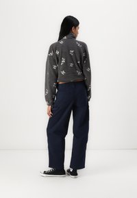 Sweater cinza, texturizado e curto com padrões florais; combinado com calças cargo largas em azul-marinho. Ténis pretos completam o conjunto.