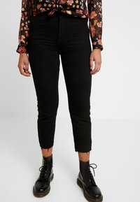 Black cropped jeans with a frayed hem, paired with black lace-up boots. The material appears denim with a slim fit design.