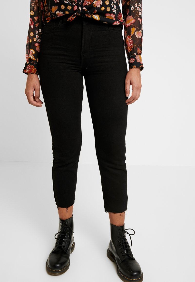 Black cropped jeans with a frayed hem, paired with black lace-up boots. The material appears denim with a slim fit design.