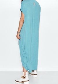 Flödig blå klänning i mjukt tyg, med rund halsringning, korta ärmar och en smyckad detalj bak. Matchad med vita platåstövlar.