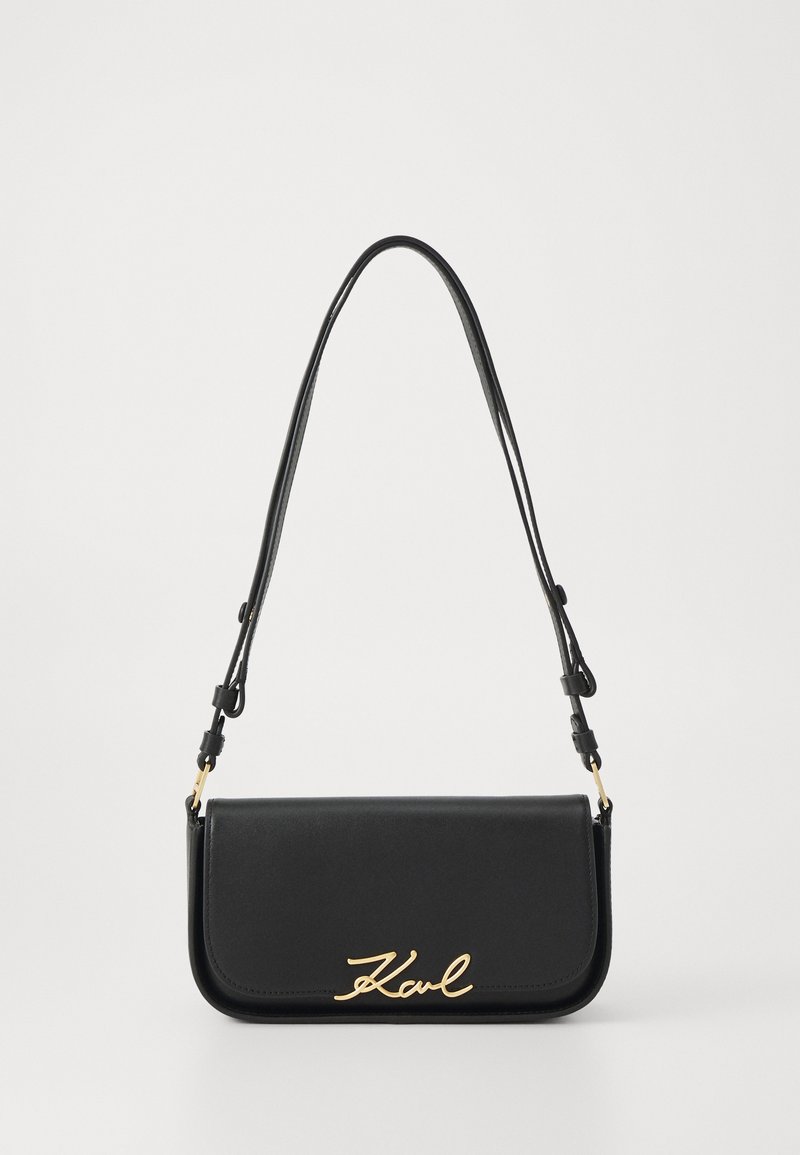 Musta nahkalaukku suorakaiteen muotoisena, jossa on kultainen kaunokirjoitettu "Karl" -logo edessä ja säädettävä hihna.