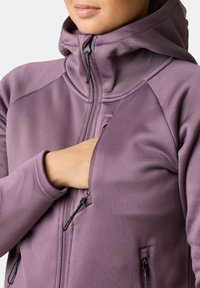 Vrouwelijke paarse jasje met hoge kraag en een volledige rits. Voorzien van zippered zijzakken en een gladde, gestructureerde stof.