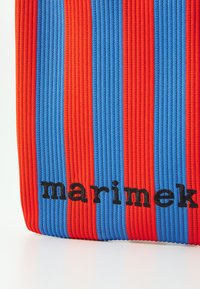 Csíkos tote táska piros és kék bordázott anyagból, fekete szöveggel, amely a táska alján a "marimekko" feliratot olvasható.