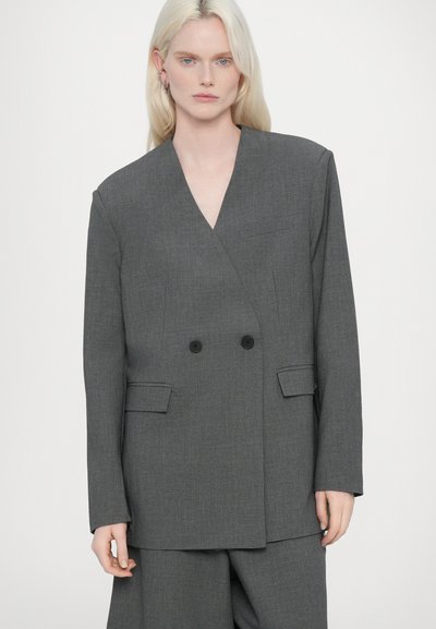 Blazer gris à double boutonnage avec deux poches avant, design structuré et revers crantés, fabriqué en tissu texturé.