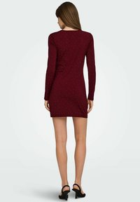 Vinröd långärmad klänning med figurnära siluett, prydd med silverprickar och hög halsringning. Kombinerad med svarta högklackade sandaler.
