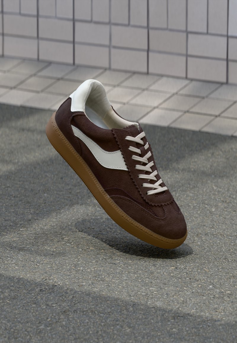 Brune semskede sneakers med hvit side stripe, flate lisser og teksturert gummisåle. Har scalloped detaljer på overdelen.