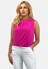 Różowa bezrękawnik z plisowanym dekoltem, wykonany z lekkiego materiału. W połączeniu z dopasowanymi białymi spodniami, które mają kieszenie z przodu.