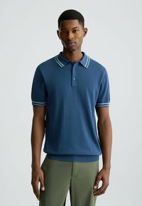 Marineblaues Polohemd mit kurzen Ärmeln, geripptem Kragen mit hellblauen Streifen, Knopfleiste und tailliertem Saum. Strukturierter Stoff.