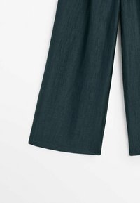 Pantalon vert foncé à jambes larges montré de mi-cuisse jusqu'à l'ourlet, mettant en valeur l'aspect texturé du tissu sur un fond blanc.