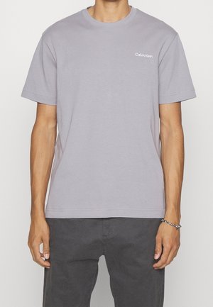 Šedé bavlněné tričko s krátkými rukávy a kulatým výstřihem, s malým bílým logem "Calvin Klein" na levé straně hrudi. Jednoduchý design, volný střih.