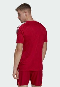 Maglia sportiva rossa con un motivo testurizzato, maniche corte e strisce bianche sulle spalle. Indossata con pantaloni corti rossi coordinati.