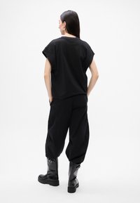 Černé oversize tričko s ohrnutými rukávy, doplněné volnými černými kalhotami a černými kozačkami po kolena. Hladká tkanina, minimalistický design.