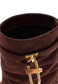 Brown suede ankle boot with a folded cuff, featuring a gold hardware buckle as a closure detail. Soft texture with a smooth interior.