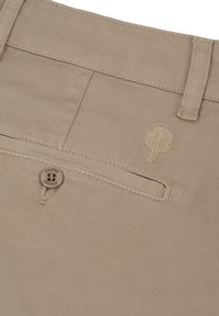 Tessuto beige con una tasca a filetto con bottone, passante per cintura e logo ad albero ricamato su un paio di pantaloni.
