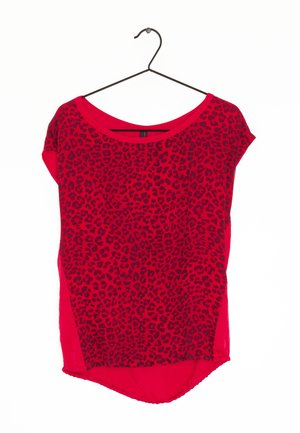 Czerwona bluzka z krótkim rękawem z czarnym wzorem w panterkę, wisząca na czarnym drucianym wieszaku na białym tle.