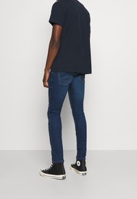Jeans slim-fit blu scuro con cuciture a contrasto e due tasche posteriori, abbinati a una maglietta nera semplice e sneaker nere alte.