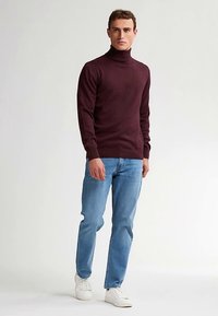 Weinroter Rollkragenpullover kombiniert mit hellblauen Jeans und weißen Sneakers. Der Pullover zeichnet sich durch eine schlanke Passform und eine weiche Textur aus.
