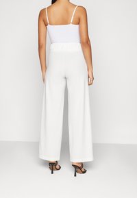 Bílé široké kalhoty s texturovaným elastickým pasem, spárované s přiléhavým bílým topem a černými sandály na podpatku.