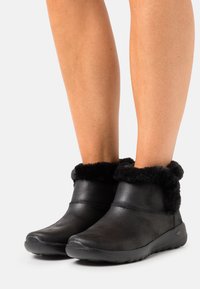 Botas negras de tobillo con un upper de cuero texturizado y un lujoso borde de piel de peluche en el cuello, con puntera redonda y suelas de goma.