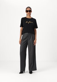 Tricou negru cu "la femme" în scris auriu; pantaloni largi gri; tocuri negre; ochelari de soare maro supradimensionați; textură de țesătură netedă.