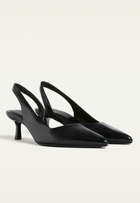 Pumps slingback neri con punta affusolata, materiale sintetico texturizzato e tacco cilindrico basso. Presentano lati tagliati eleganti.