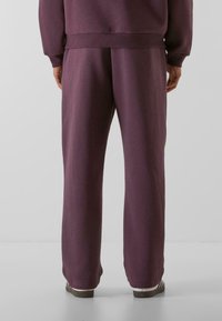 Lilla bomulds sweatpants med en afslappet pasform, der har en elastisk talje og let tilspidsede ben, vist fra bagsiden.