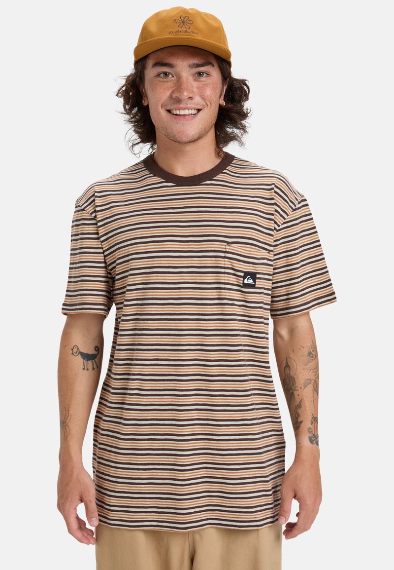 Camiseta de manga corta a rayas en marrón, crema y tostado; presenta un bolsillo con un parche de logo. Tejido texturizado. Se lleva con una gorra tostada.