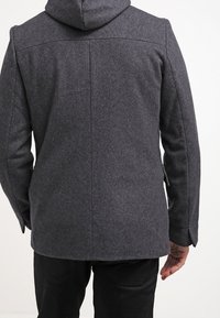 Cappotto di lana grigio con cappuccio, caratterizzato da un taglio dritto, maniche lunghe e linee pulite. La vista posteriore mostra dettagli di cucitura semplici.