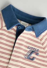 Koszulka polo z niebieskim kołnierzykiem i guzikiem, uszyta z kremowego materiału w czerwone paski, z haftem "LITTLE C" w kolorze niebieskim.