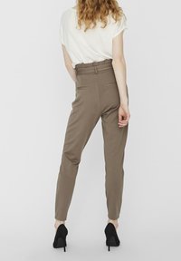 Hoge taille, slim-fit broek van lichtbruin materiaal, met twee achterzakken en een gladde textuur, in combinatie met zwarte hoge hakken.