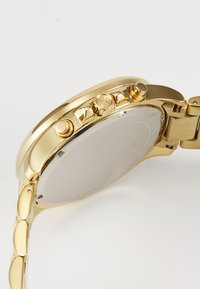 Goldfarbenes Edelstahlarmband mit rundem Zifferblatt, drei Druckknöpfen an der Seite und einem verlinkten Armband mit glatten, ovalen Gliedern. Schlichter Gehäuseboden.