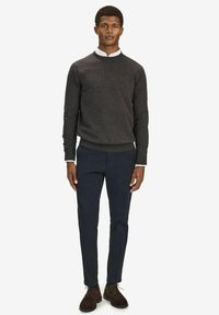 Grå tröja med rund halsringning, marinblå byxor och bruna mockaskor. Modellen står upprätt med händerna synliga, neutral bakgrund.