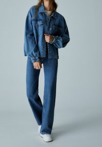 Chaqueta de mezclilla con un corte relajado y mangas abullonadas, combinada con jeans de tiro alto y pierna ancha. Ambas prendas son de un lavado en azul claro.