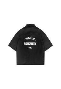 Chemise noire à manches courtes avec texte blanc brodé "Atelier RETERNITY 7/7" au dos, présentée à plat sur fond blanc.