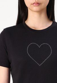 Svart bomull T-skjorte med et hjerteformet design laget av sølvstrass i midten, med klassisk rund hals og korte ermer.