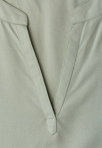 Tissu vert clair avec un décolleté en V profond, présentant des revers cousus et un petit détail de languette au bas du centre du décolleté.