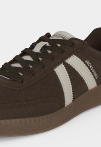 Baskets en daim marron avec des bandes crème, des lacets foncés et le logo "JACK & JONES" sur le côté, présentées sur un fond uni.