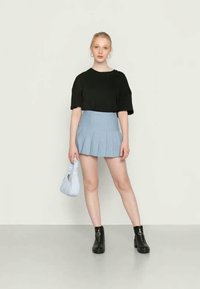 Top preto oversized de mangas curtas, saia mini plissada azul clara, botas pretas de tornozelo com detalhes circulares e uma bolsa azul clara.