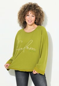 Sweat-shirt vert olive avec une coupe décontractée, encolure ronde et manches longues. Embellit d'une broderie argentée avec "Liberté EST. 1987". Manches accentuées.