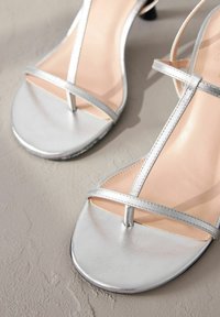 Zilveren bandjes sandalen met een platte zool en T-band ontwerp. Glad metallic oppervlak en minimalistische stijl met een lichtroze interieur.