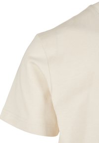 Manche courte d'un t-shirt en coton beige uni montrant la texture du tissu et les détails des coutures sur fond blanc.