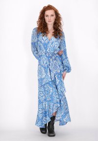 Maxime-mekko sinisenä, jossa on monimutkainen paisley-kuvio, pitkät hihat, kietaisumalli ja levenevä helma. Tyylitelty mustilla nilkkasukilla.