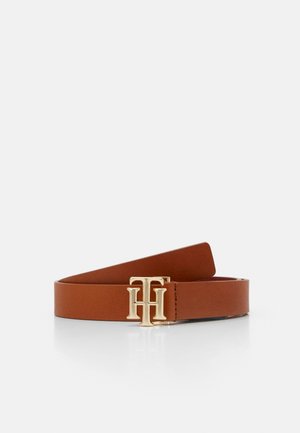 Ceinture en cuir marron avec une boucle en métal doré présentant les lettres entrelacées T et H, reposant sur une surface blanche.