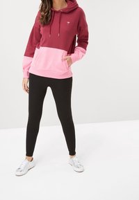 Maroon and pink color-blocked hoodie with a front pocket, adjustable hood, and white logo. Paired with black leggings and silver sneakers.