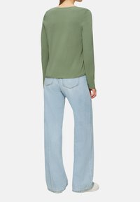 Langärmliges, Rundhals-Top aus weichem olivgrünem Stoff, kombiniert mit hellblauen, weit geschnittenen Jeans mit klassischem Fünf-Taschen-Design.