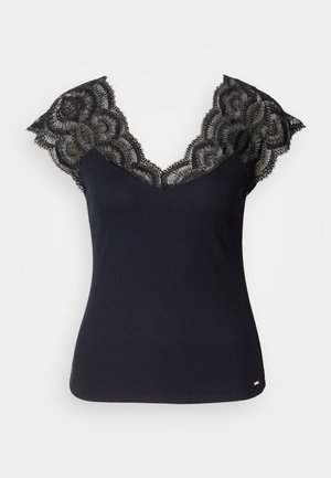 Black ribbed tank top featuring a deep V-neck with lace detailing at the shoulders and scalloped edges. Minimal hardware accents at the hem.