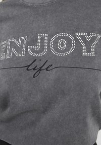 Sivá mikina so ozdobami z kamienkov, na ktorej je napísané "ENJOY" a čiernym kurzívnym písmom "life" pod ním. Má voľný strih a mäkkú textúru.