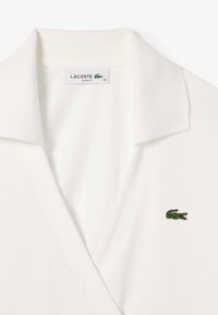 Polo shirt slim-fit bianco Lacoste con colletto a punta e un piccolo logo coccodrillo verde sul lato sinistro. Tessuto liscio.