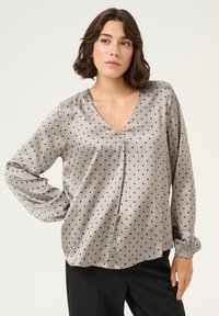 Silk blouse in light gray with black polka dots. Features a V-neckline, long sleeves with elastic cuffs, and a relaxed fit.